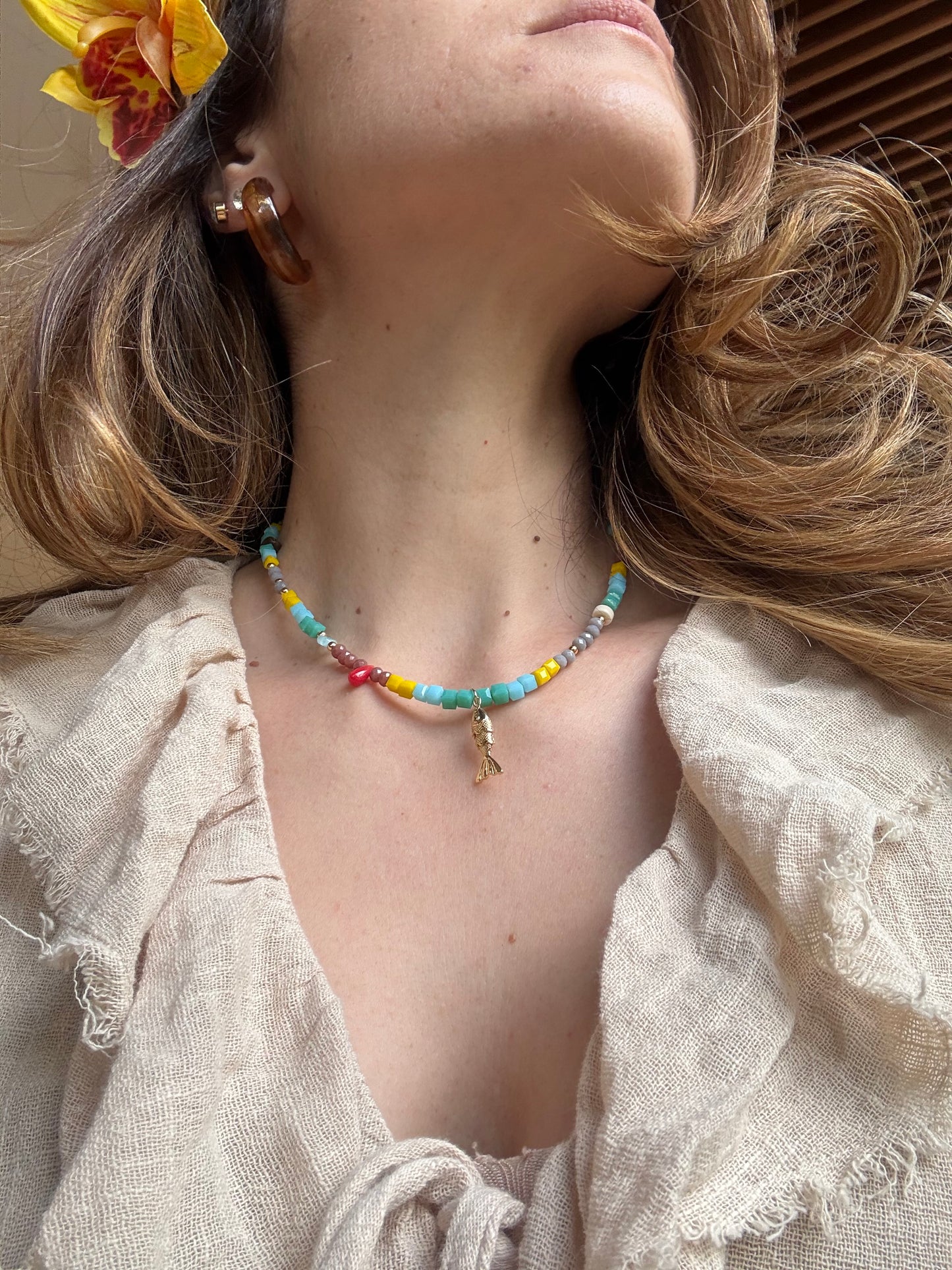 Collar corto en piedras con dije en forma de pez rodinado.